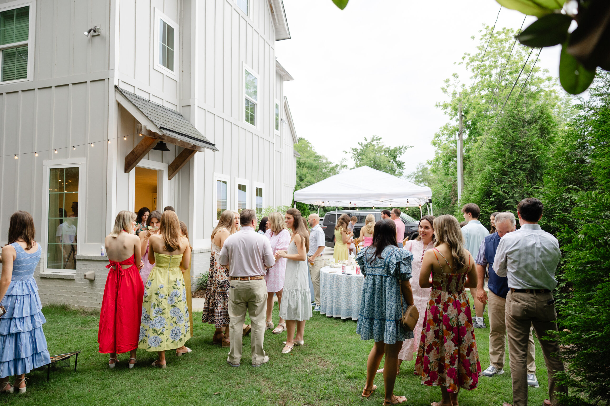 Outdoor graduation party with guest mingling under a white tent decorated with beautiful tablecloths